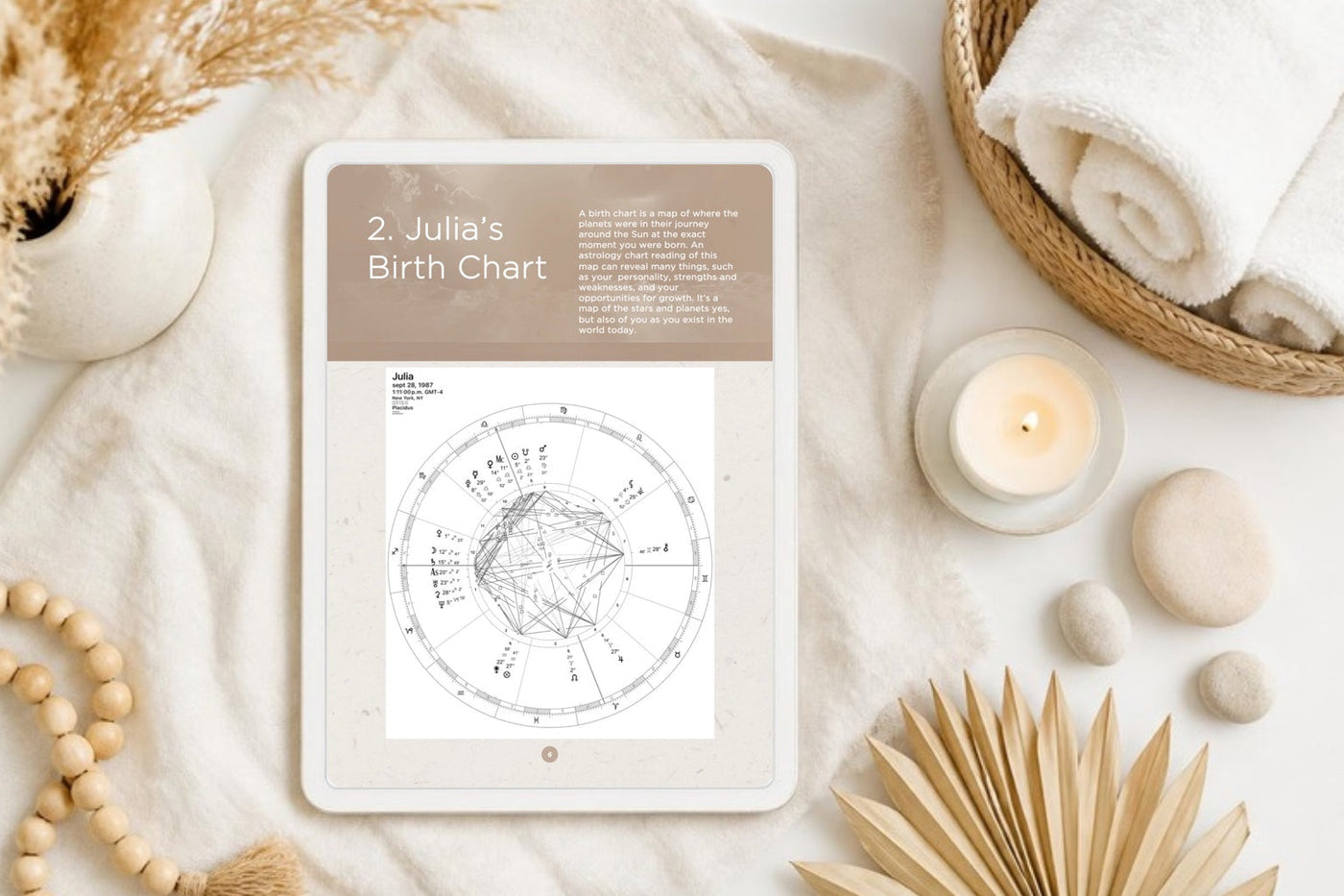 A personalized birth chart guide on a cream tablet in a calm spa setting with a candle, towels and dried flowers