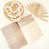 Printed parenting guide open on the sign modality page, with wooden beads and a dried palm leaf